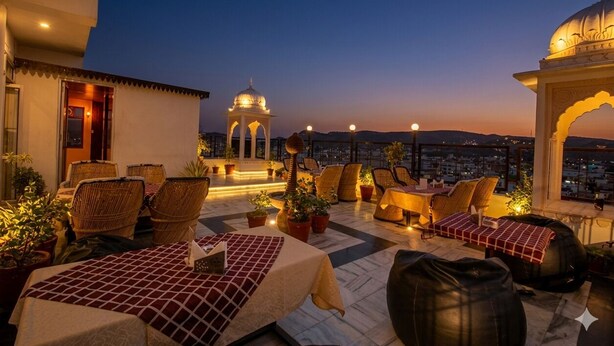 A rooftop terrace with seating, potted plants, and a view of the cityscape at dusk. - Amer City Heritage Hotel (Jaipur)