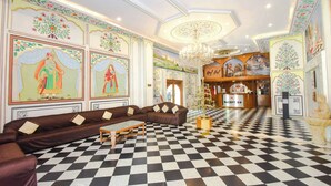 A hotel lobby with a checkered floor, a reception desk, and traditional artwork on the walls. - Amer City Heritage Hotel (Jaipur)