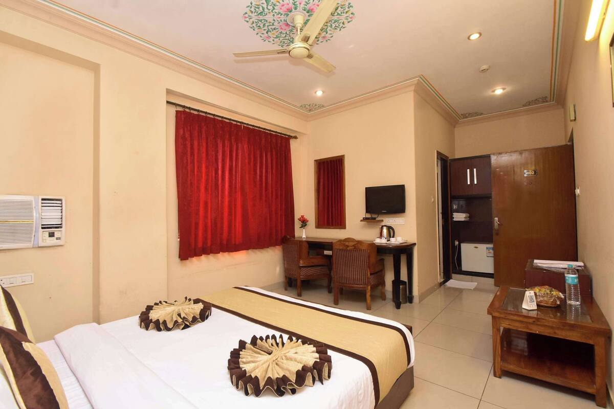 Ein Hotelzimmer mit Bett, Schreibtisch, Stuhl und einem kleinen Tisch mit einer Wasserflasche und einer Tasche.