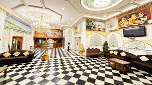 A hotel lobby with a checkered floor, ornate wall decorations, a chandelier, and seating areas. - Amer City Heritage Hotel (Jaipur)
