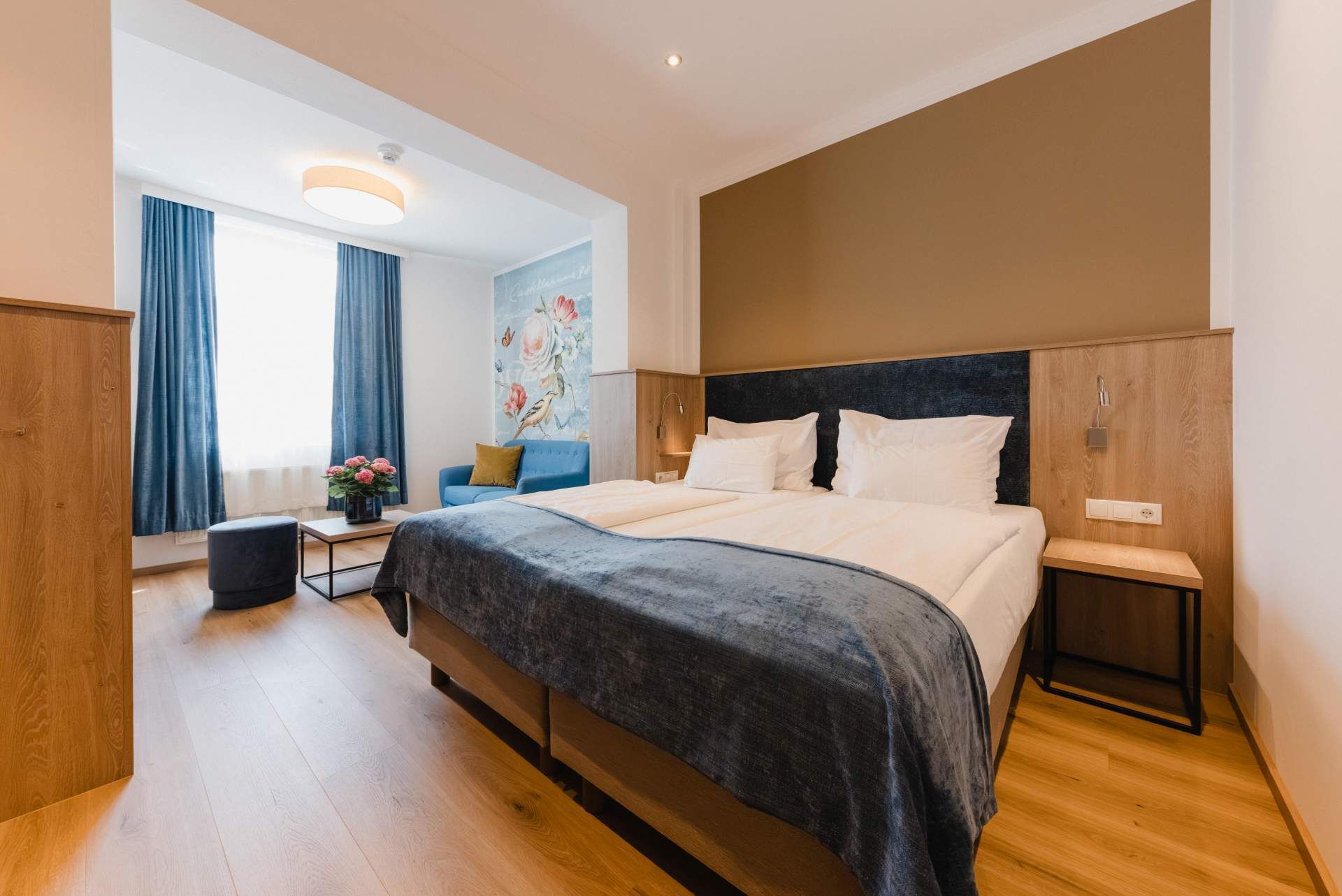 A modern hotel room with a large bed, a small seating area, and a view of the outdoors.