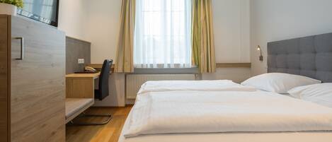 A hotel room with a bed, a desk with a chair, a TV, and a window with curtains.
