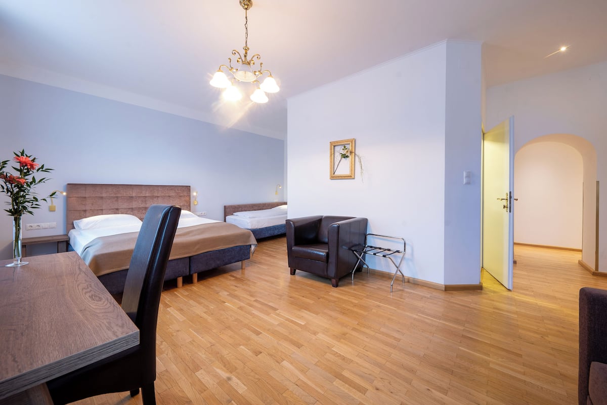 Une chambre d’hôtel moderne avec un plancher en bois, deux lits simples, une table à manger avec des chaises, une télévision et un petit coin salon.