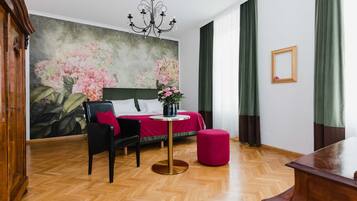 Ein Hotelzimmer mit einem Bett, einem Schreibtisch, einem Stuhl, einem Tisch, einer Kristallleuchter und einer großen Blumenmalerei an der Wand.