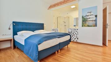 A bedroom with a bed, bedside table, wooden floor, and a bathroom with a shower and a mirror.