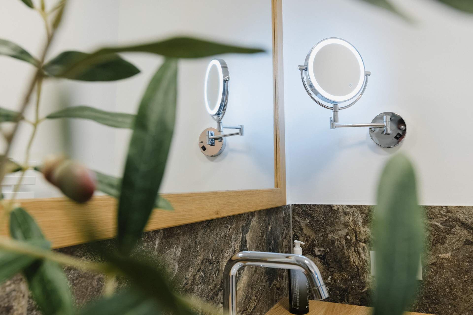 A bathroom with a marble countertop, a sink, a mirror with a light, and a plant.