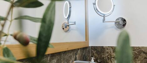 A bathroom with a marble countertop, a sink, a mirror with a light, and a plant.
