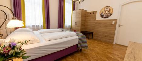A bedroom with a bed, a nightstand, a dresser, a bench, a chandelier, and a door.