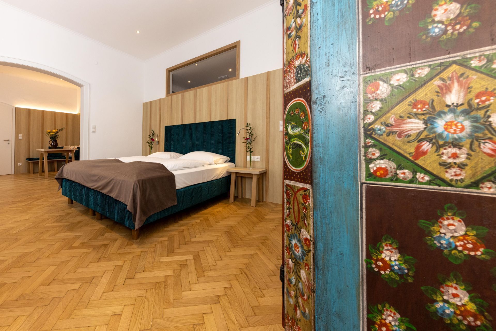 A bedroom with a bed, wooden floor, and a wall with floral wallpaper.