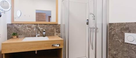 A modern bathroom with a glass-enclosed shower, a wooden vanity with a sink and mirror, and a marble backsplash.