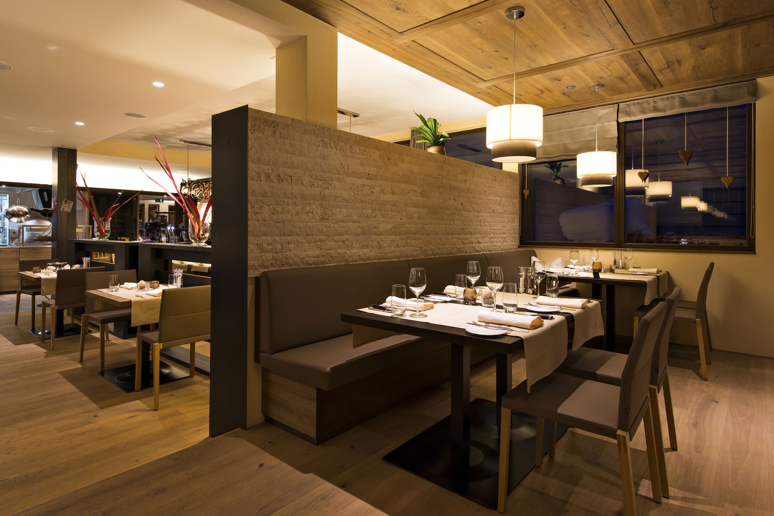 A modern restaurant with wooden flooring, a central seating area with a bench, and tables set for dining.