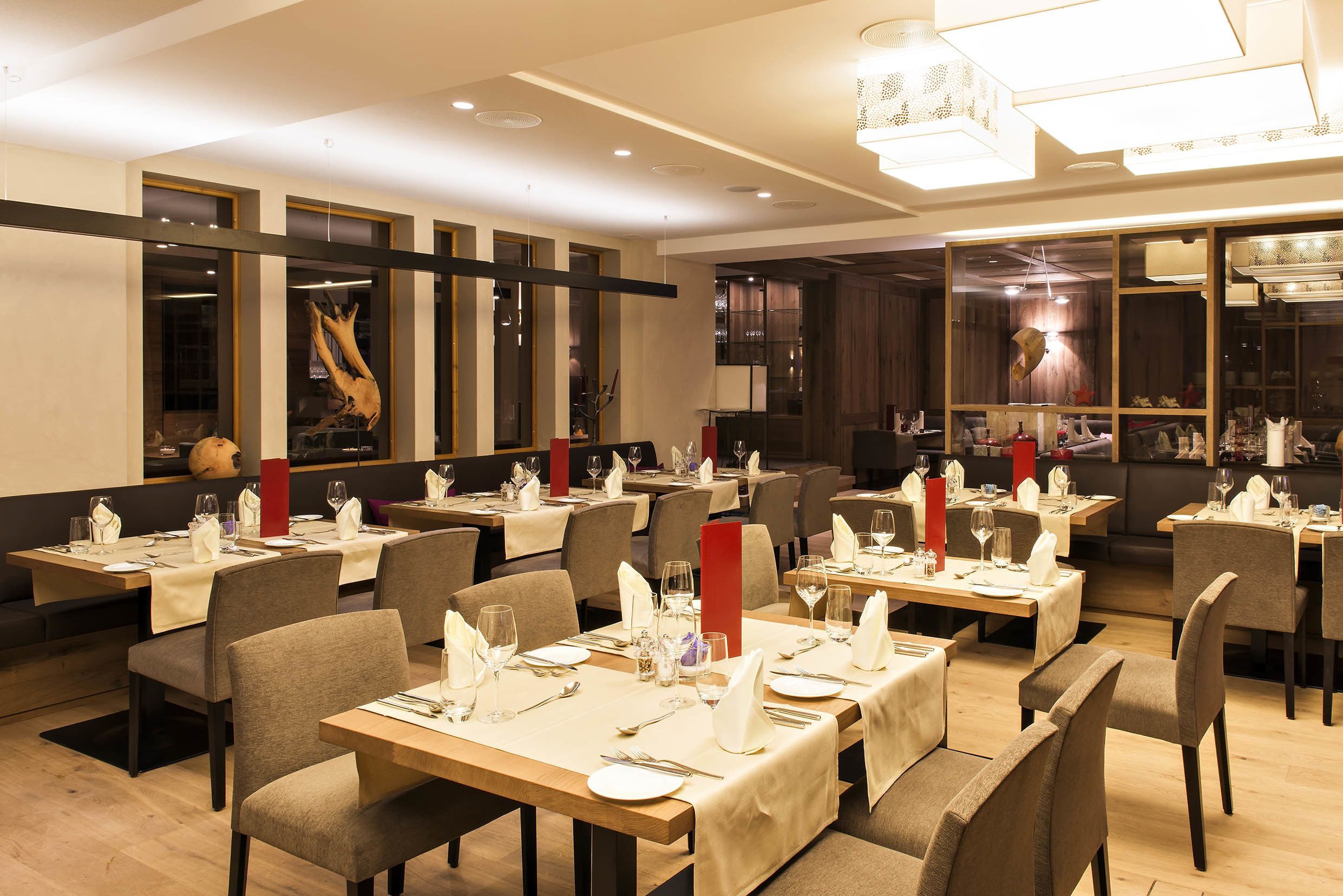 Un restaurante con varias mesas dispuestas para comer, con una decoración interior moderna, suelo de madera y mobiliario contemporáneo.