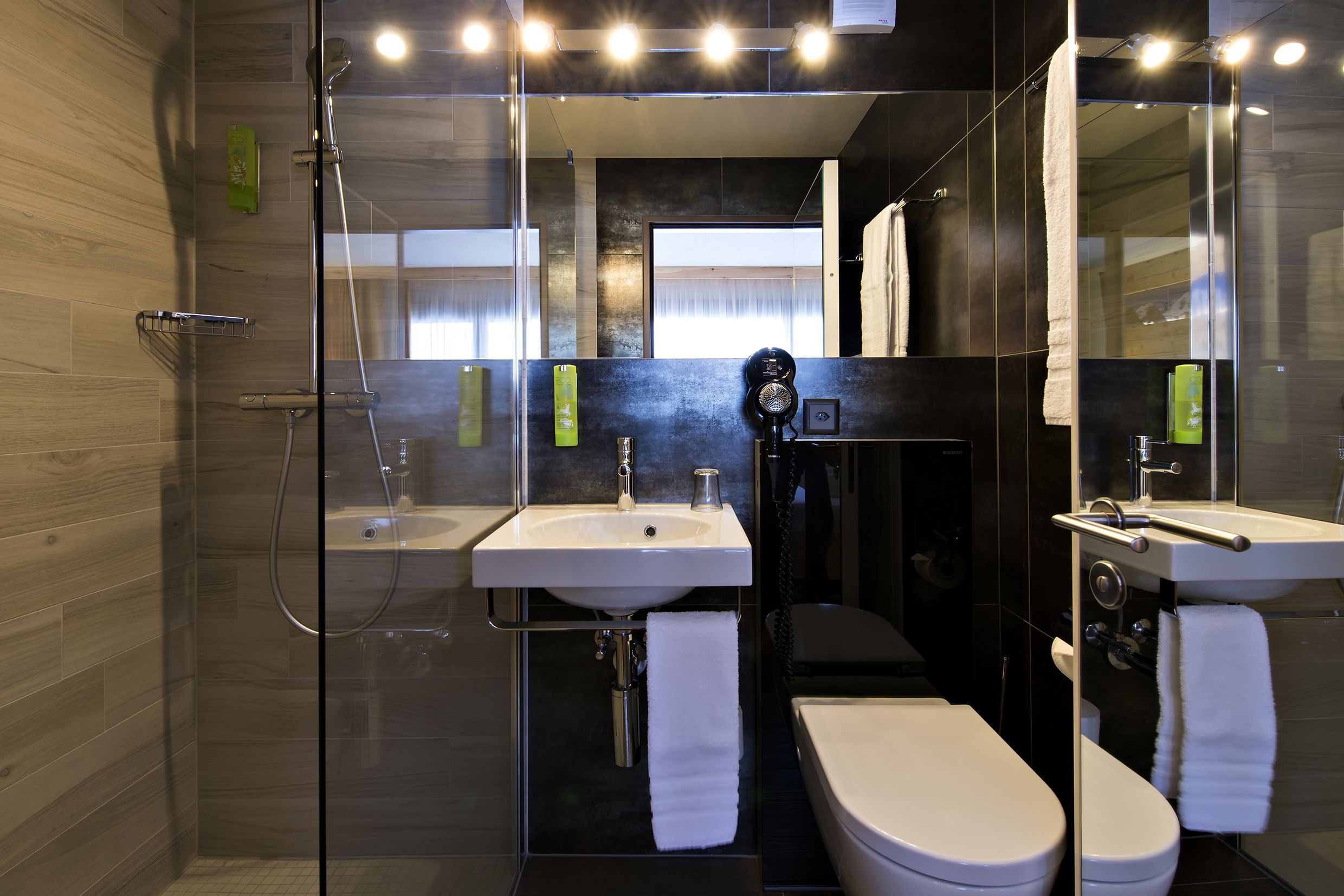Un baño moderno con cabina de ducha de vidrio, dos lavamanos y un inodoro.