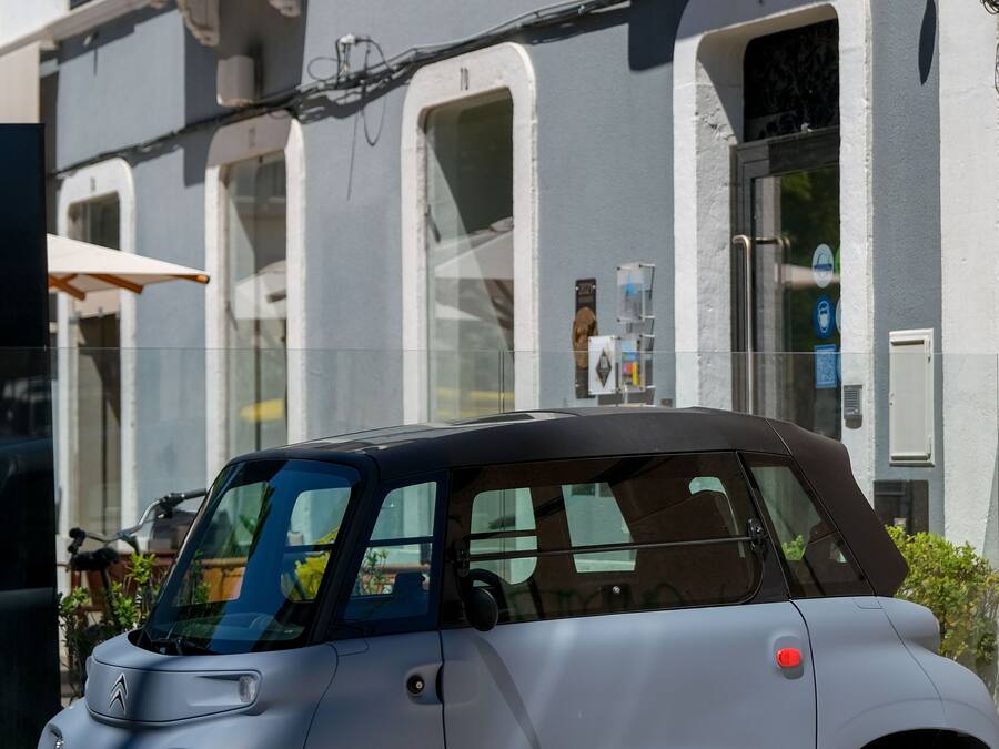 A compact car parked in front of a building with a balcony and a door.