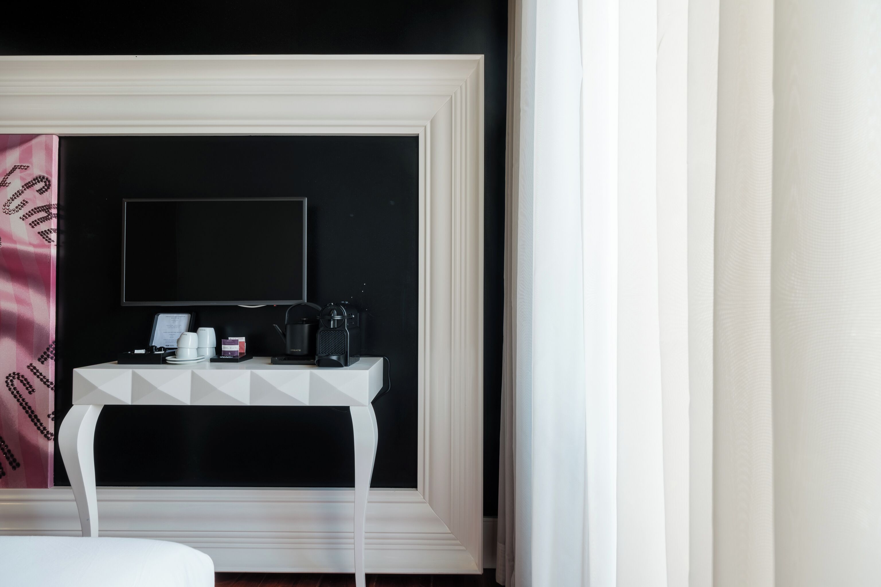 A room with a white console table, a flat-screen TV, and a coffee machine.