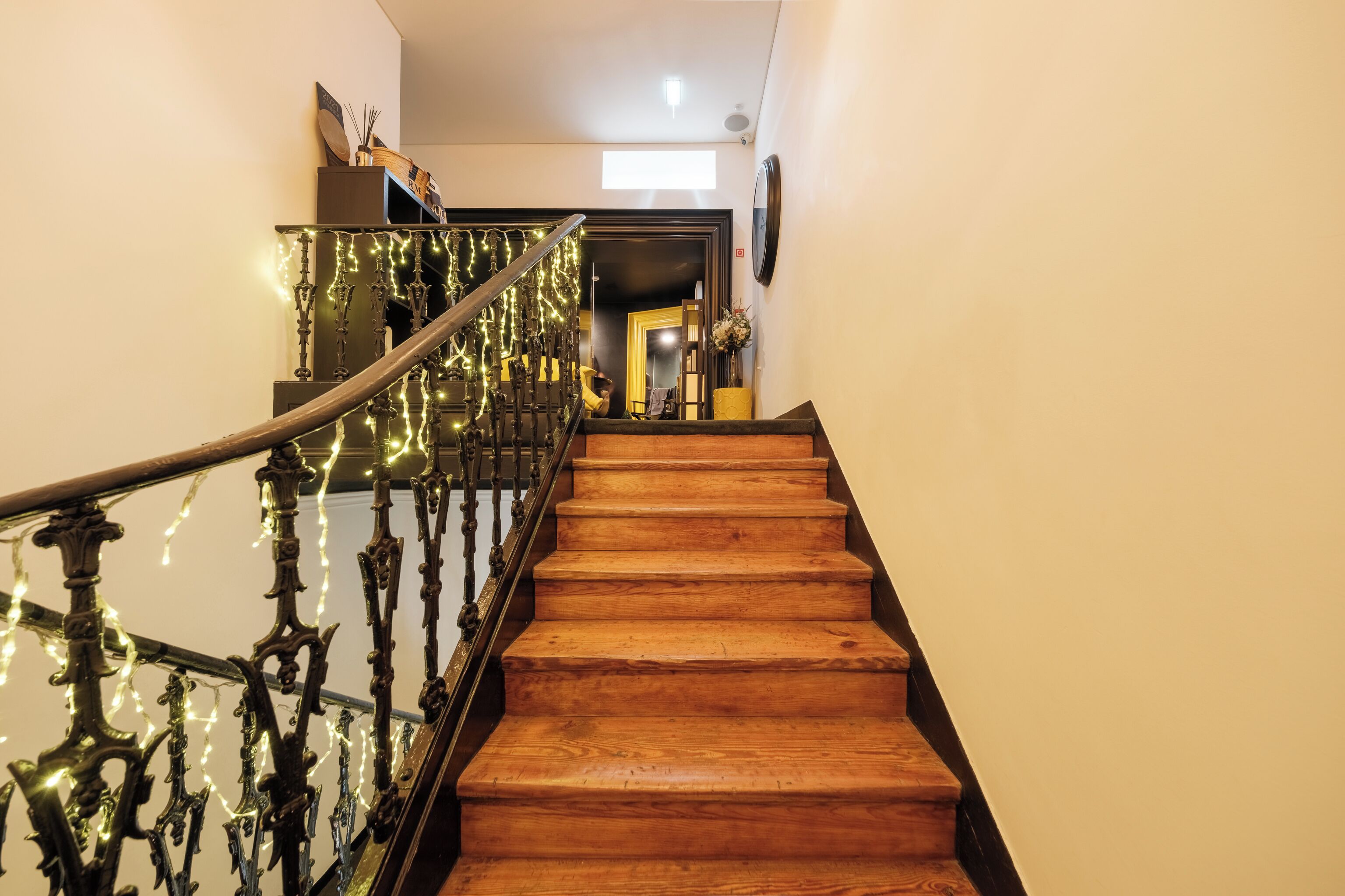 A wooden staircase with a metal railing, leading to a room with a bed and a nightstand.