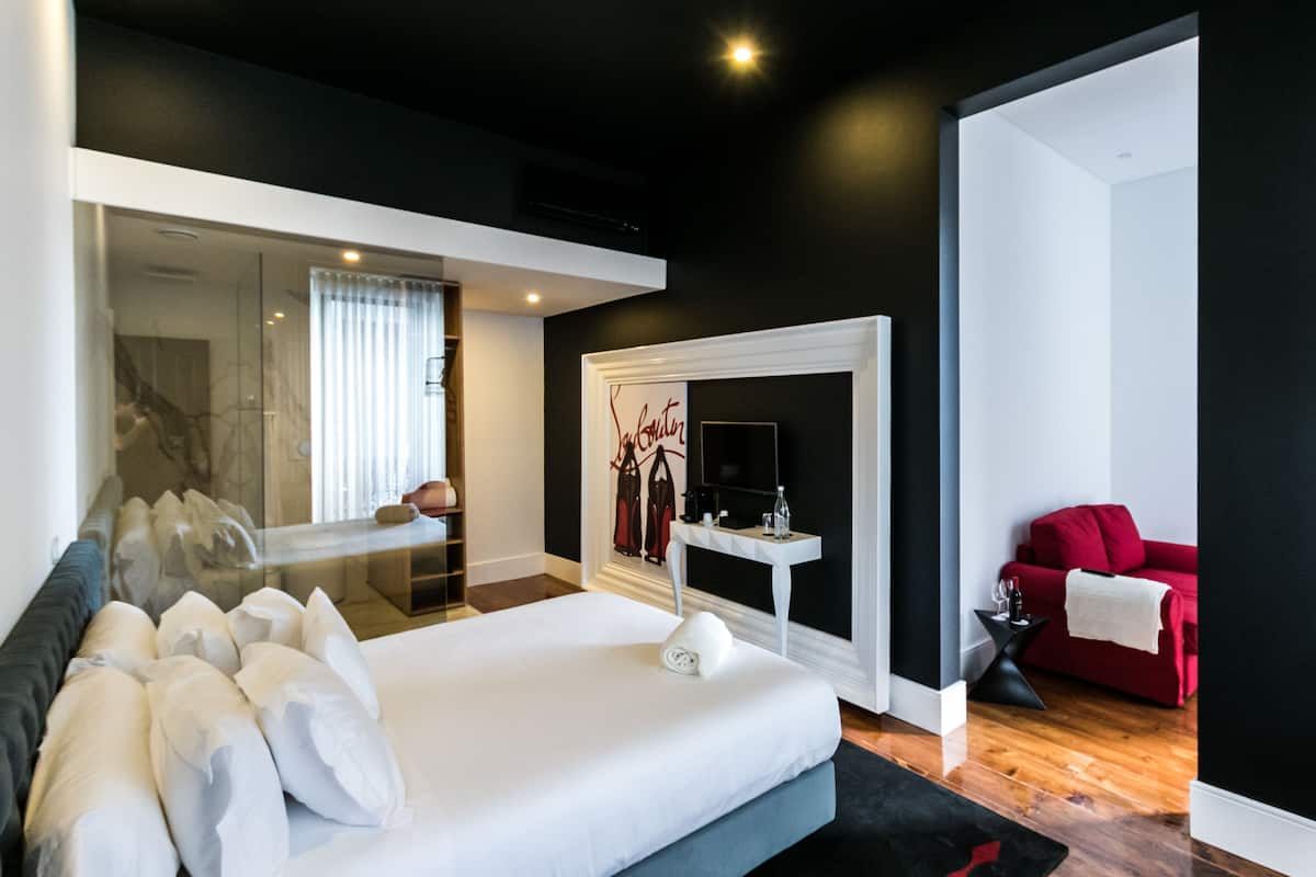 A modern hotel room with a large bed, a red sofa, a small side table, and a mirror.