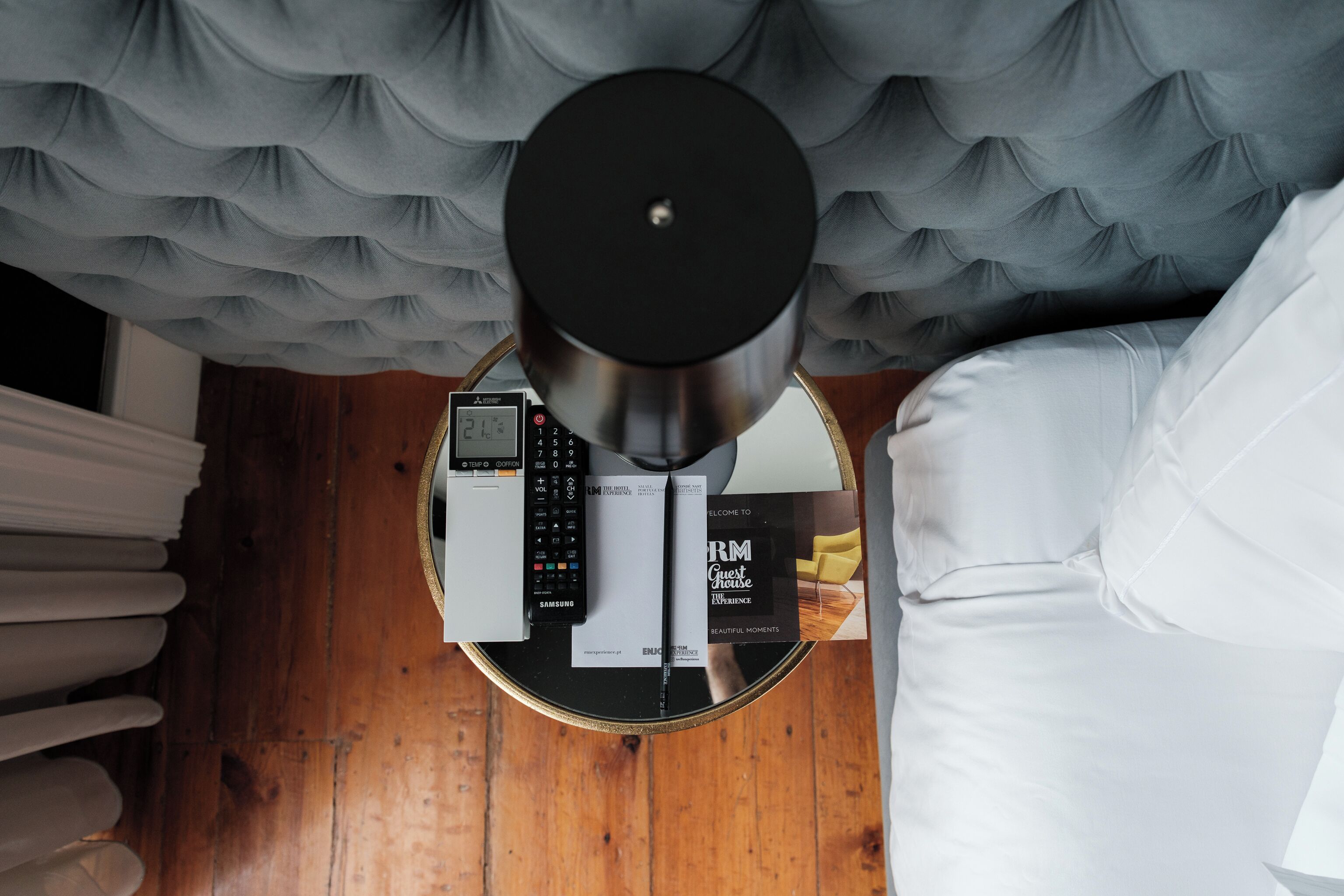 Una habitación con una cama, una mesa redonda con un objeto negro encima, un control remoto y un libro titulado 'RM Guest House'.