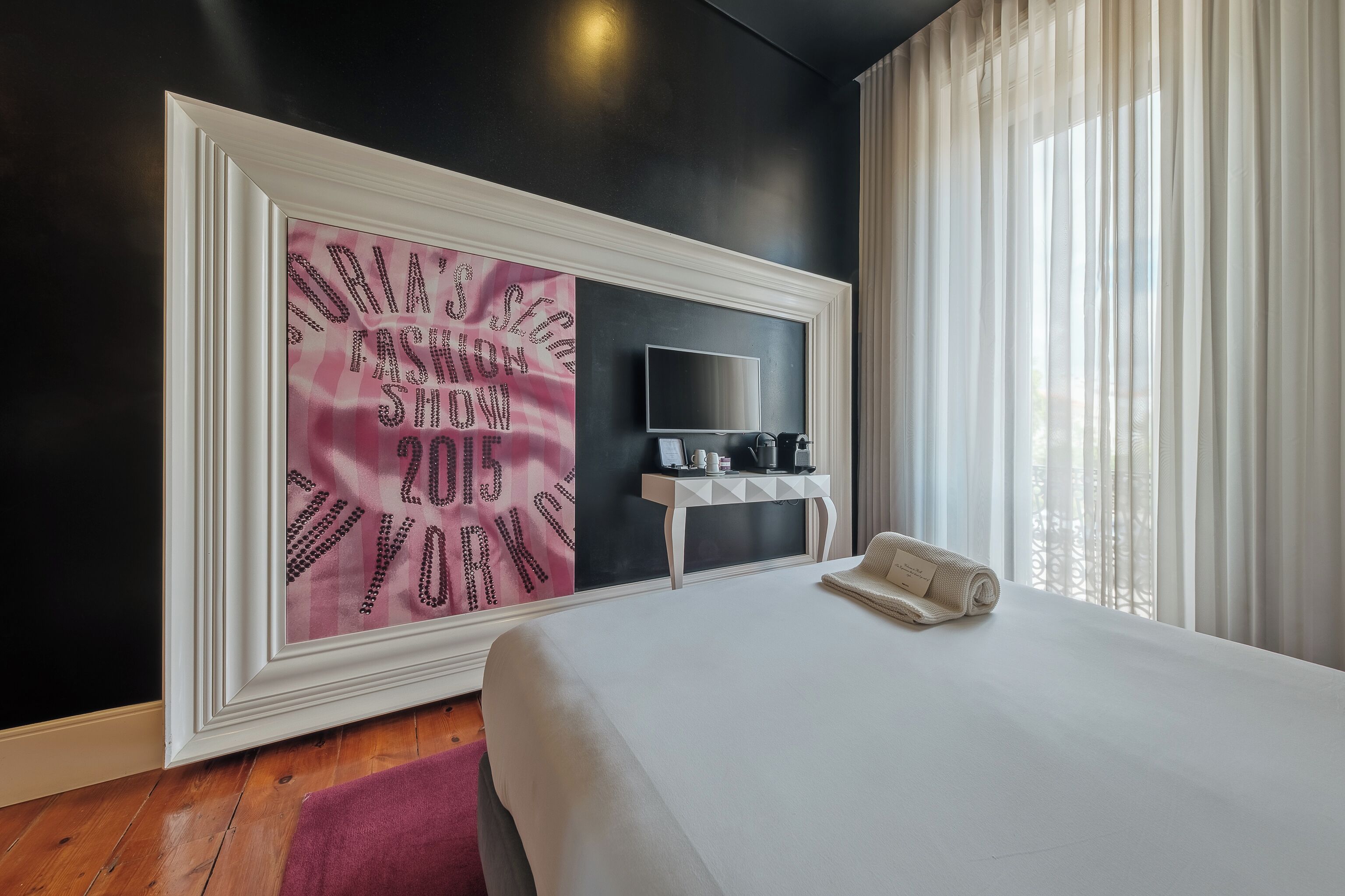 A hotel room with a large framed artwork, a flat-screen TV, a bedside table with a coffee maker, and a neatly made bed.