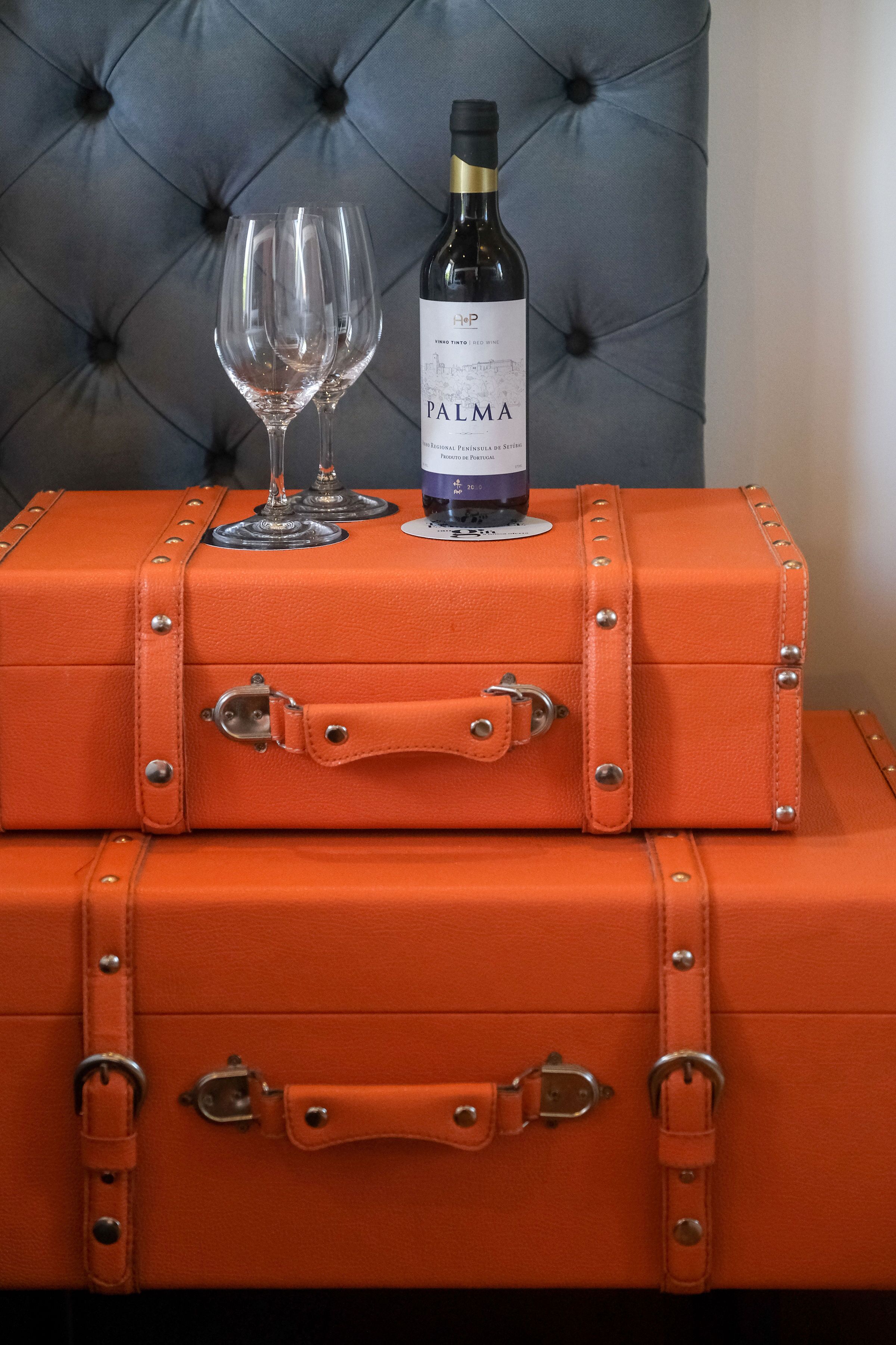 A stack of orange leather suitcases with metal clasps and a bottle of wine and a glass on top.