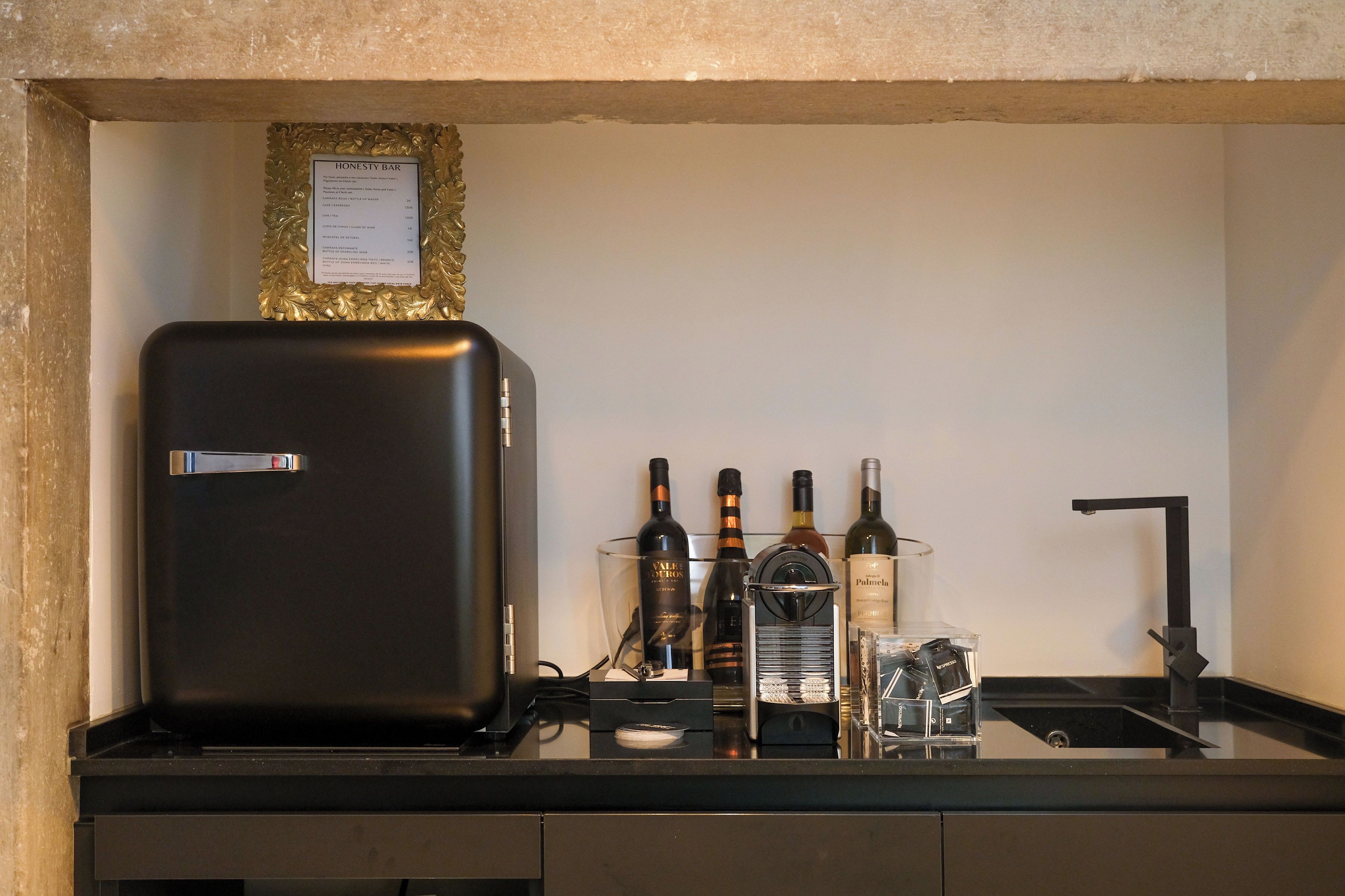 Eine Bar mit einem schwarzen Kühlschrank, Weinflaschen, einer Karaffe und einer Speisekarte an der Wand.