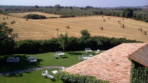 Vista de una propiedad en el campo con césped, mobiliario exterior y pacas de heno al fondo.