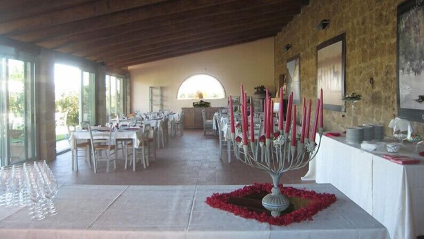 Un comedor interior con mesas dispuestas para una comida, una pieza decorativa central y una pared de piedra con un cuadro enmarcado.