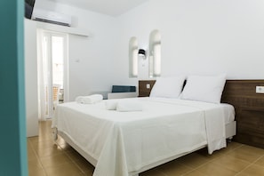 A hotel room with a large bed, a bedside table, a wall-mounted air conditioner, and a door leading to a balcony. - Kissamia - Self Check In Only - Next to Night Clubs (Kissamos)