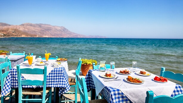 A seaside dining area with checkered tablecloths, outdoor seating, and a view of the sea and hills. - Kissamia - Self Check In Only - Next to Night Clubs (Kissamos)