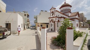 A white building with a red-tiled roof and a dome, surrounded by a paved street and a parked car. - Kissamia - Self Check In Only - Next to Night Clubs (Kissamos)