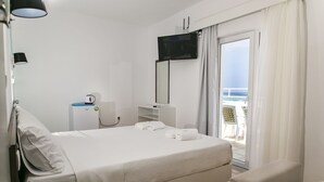 A hotel room with a bed, a TV, a desk with a computer, a chair, and a balcony with a view of the sea. - Kissamia - Self Check In Only - Next to Night Clubs (Kissamos)