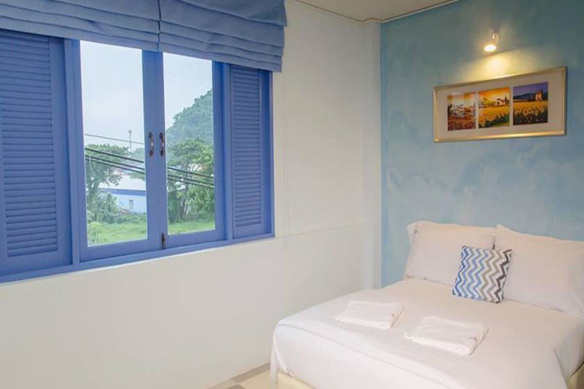 Quarto com cama, janela com persianas azuis e quadro na parede.