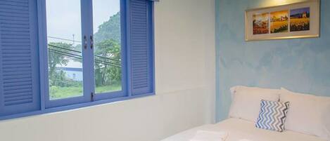 A bedroom with a bed, a window with blue shutters, and a framed picture on the wall.