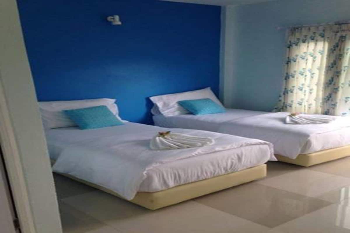 Quarto de hotel com duas camas, cada uma com roupa de cama branca e um travesseiro azul.