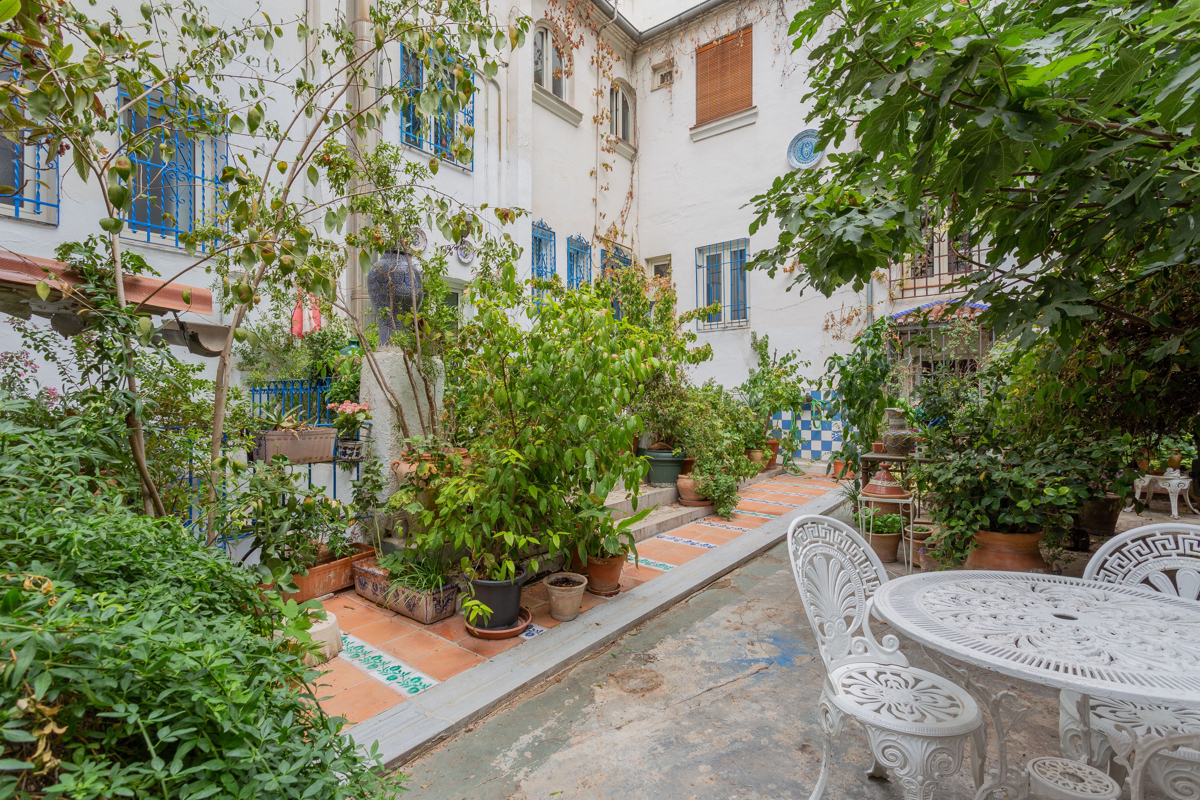 A courtyard with potted plants, a tiled floor, and white outdoor furniture.