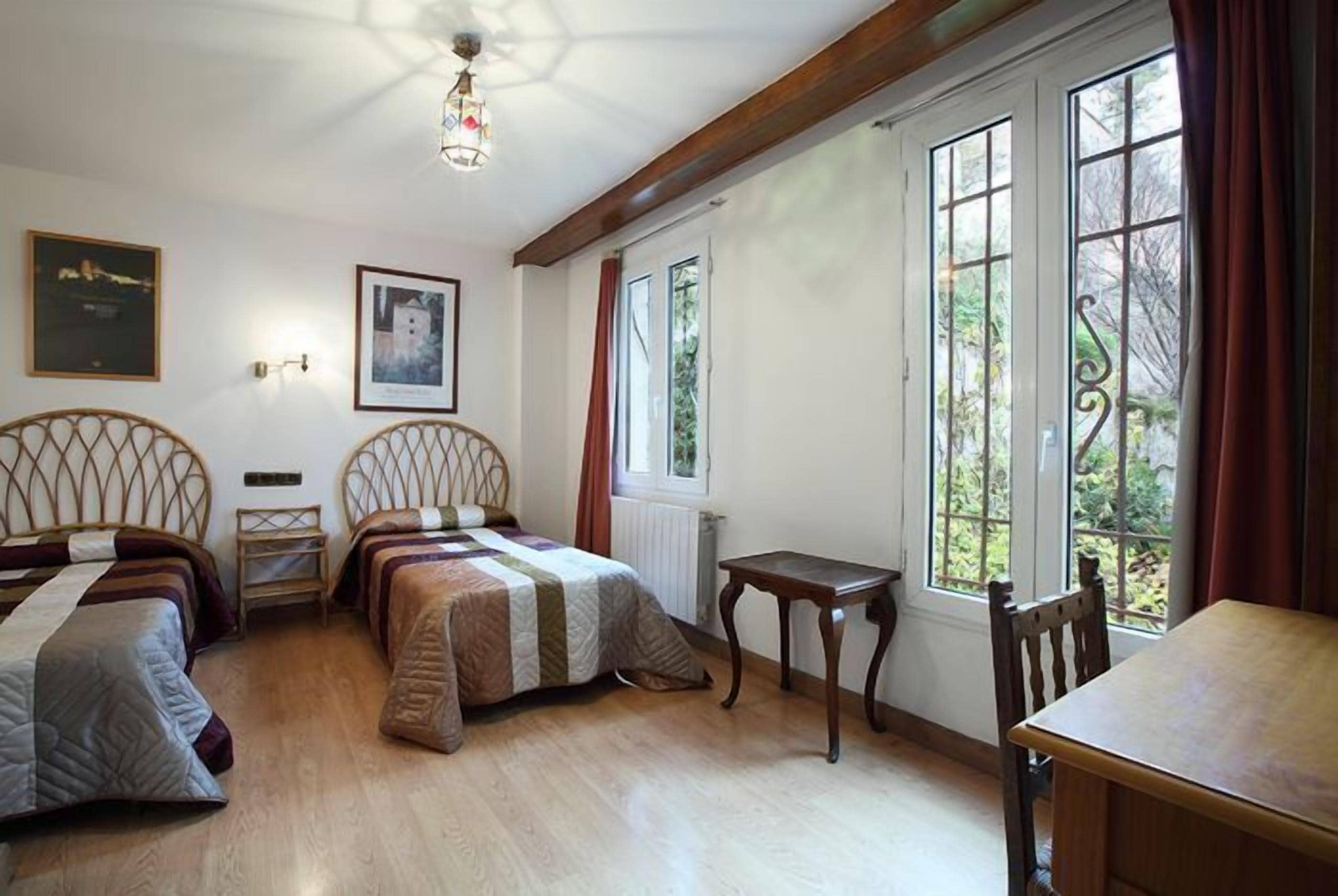 A bedroom with two beds, a small table, and a window with curtains.