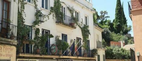 Una calle con un café y un bar, un edificio con el letrero 'Pension Landazur', y algunas personas caminando.