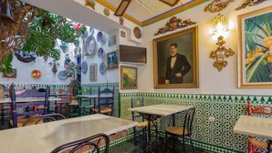 A restaurant interior with traditional decor, including patterned tiles, hanging plants, and framed artwork on the walls. - Pensión Landazuri (Granada)