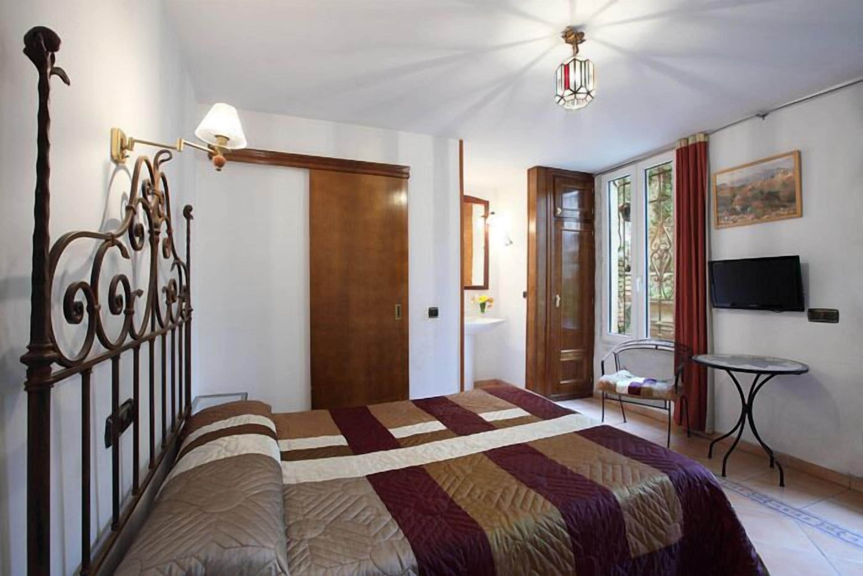 A bedroom with a bed, a bedside table, a chair, a TV, and a door.
