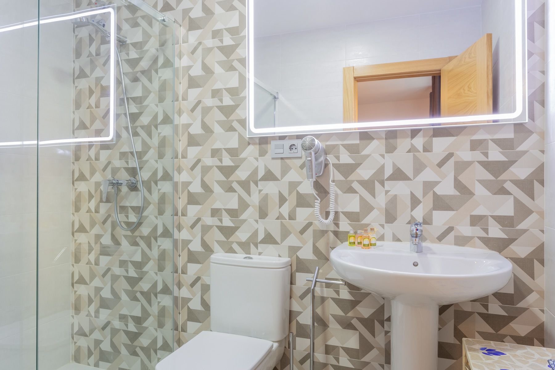 Un baño con ducha, inodoro y lavamanos, todo con baldosas de diseño geométrico.