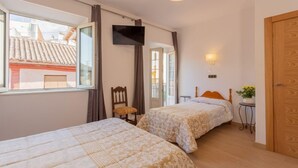 A bedroom with two beds, a TV, a small table with a plant, and a door. - Pensión Landazuri (Granada)