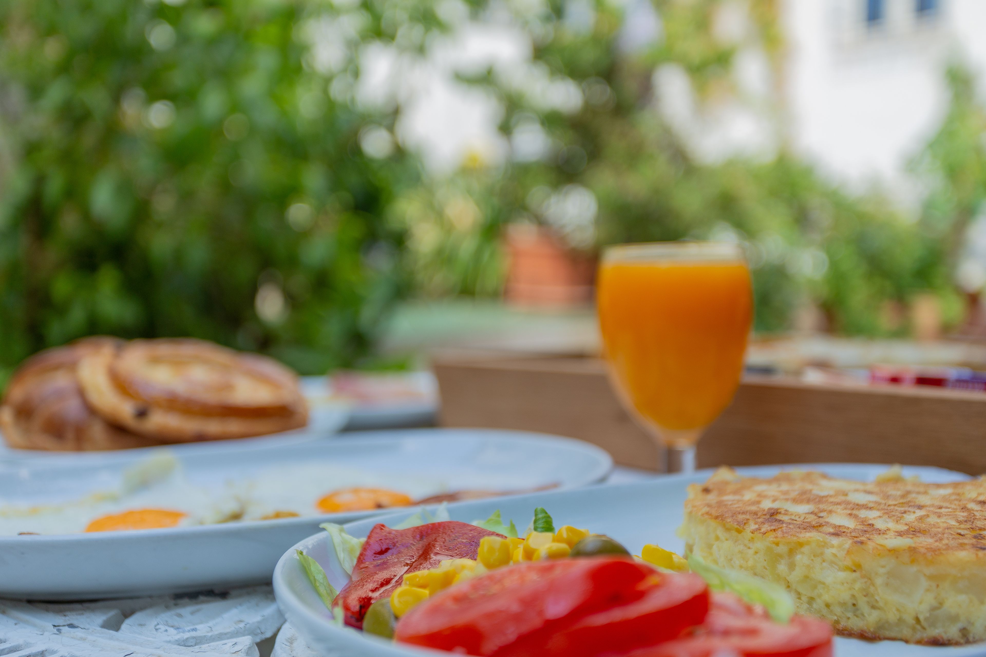 A breakfast setting with plates of food, including eggs, toast, and a glass of orange juice, on a table outdoors.
