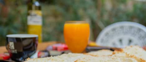 A breakfast setting with bread, a cup, a glass of orange juice, and a bottle of olive oil on a wooden table.
