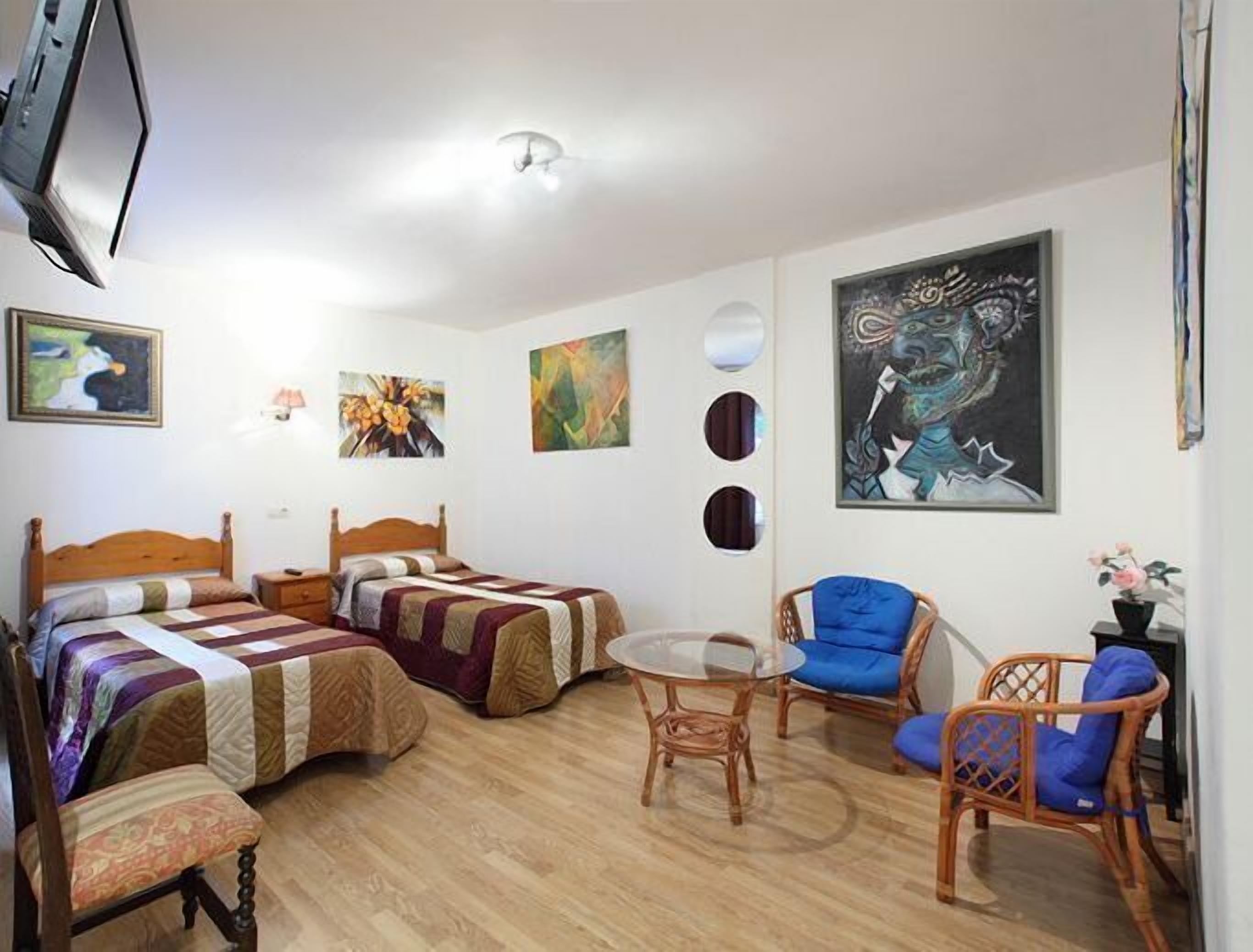 A room with two beds, a round table, and wicker chairs.