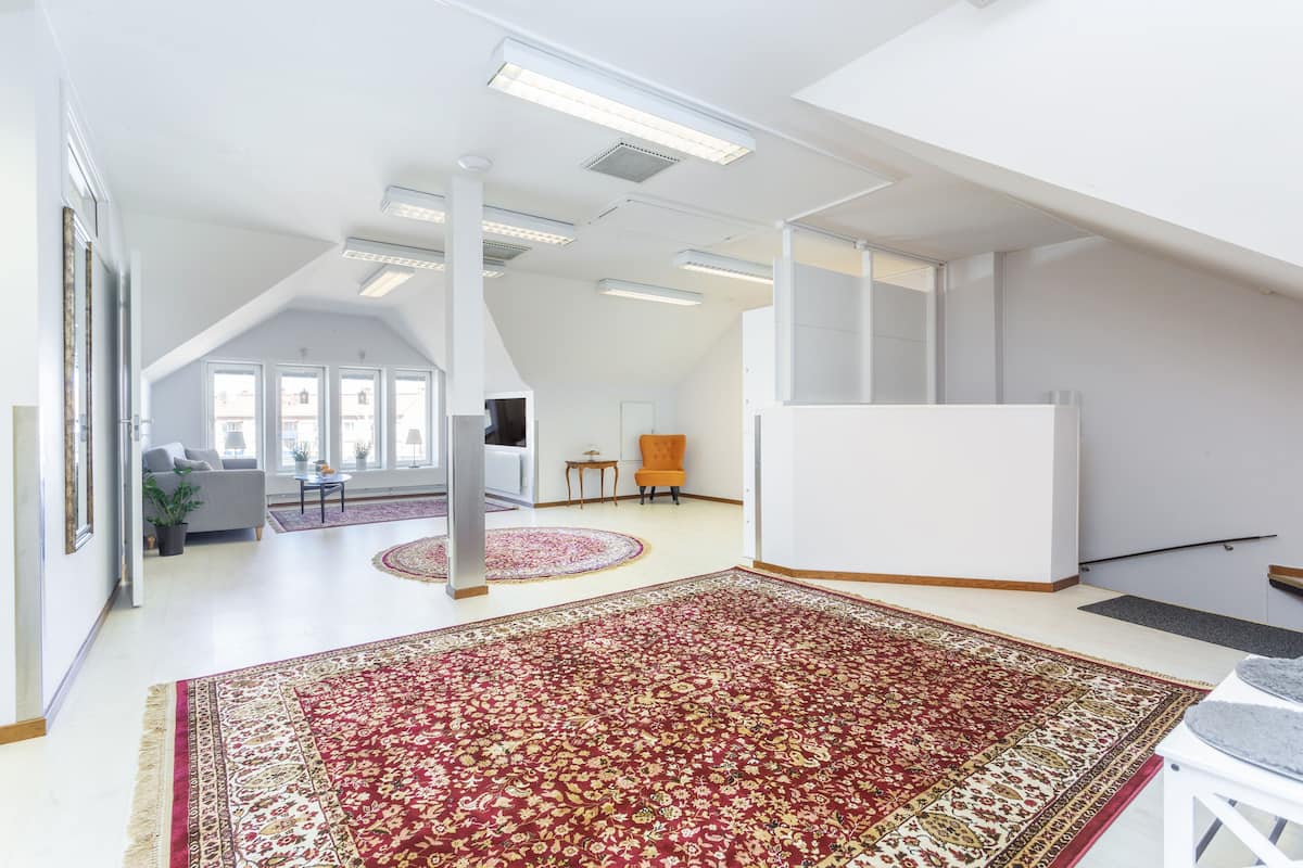 A spacious loft with high ceilings, large windows, and a red patterned carpet.