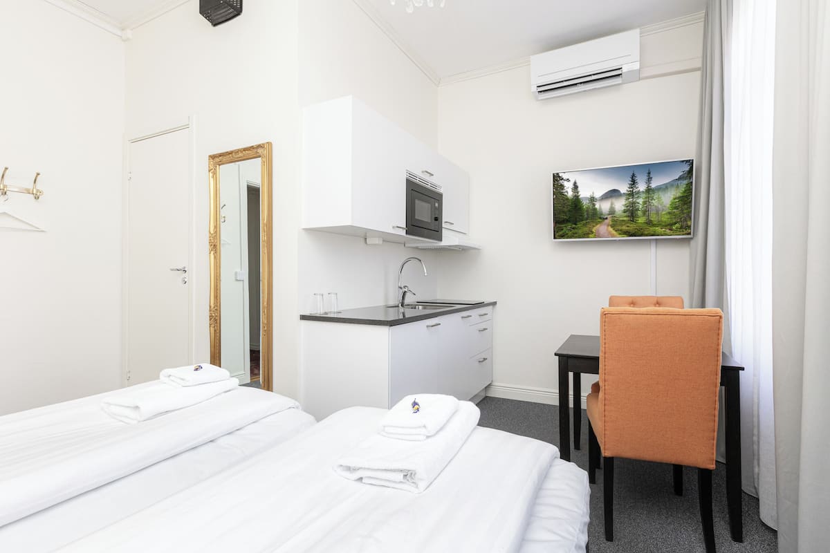 A hotel room with two beds, a small kitchenette, a desk, and a TV.