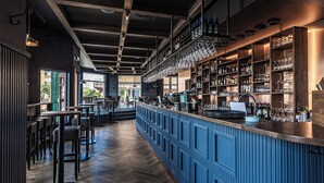 Una zona de bar con una barra larga, taburetes y estantes llenos de botellas y vasos.