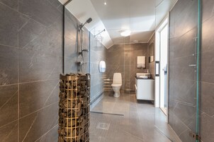 Un baño moderno con ducha envuelta en cristal, un pilar de piedra y un área de aseo separada.