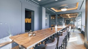 Un comedor moderno con una larga mesa de madera, varias sillas y una cocina a la vista al fondo.