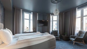 Un cuarto de hotel con una cama grande, televisión, candelabro y vista de la ciudad.